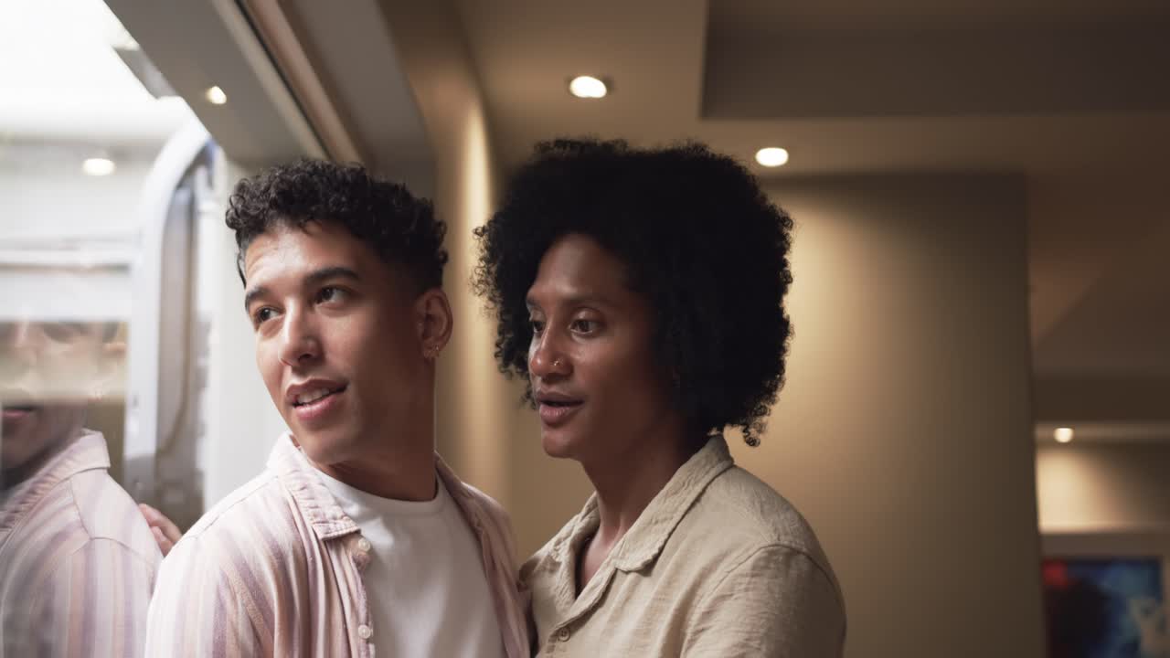 Diverse male duo standing by window, lighter man spotting outside and pointing, darker man leaning