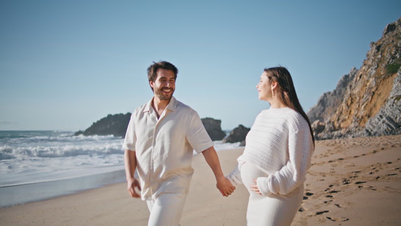 임신 한 커플 이 해변 을 산책 하고 빛 이 있는 자연 을 즐기고 있다.