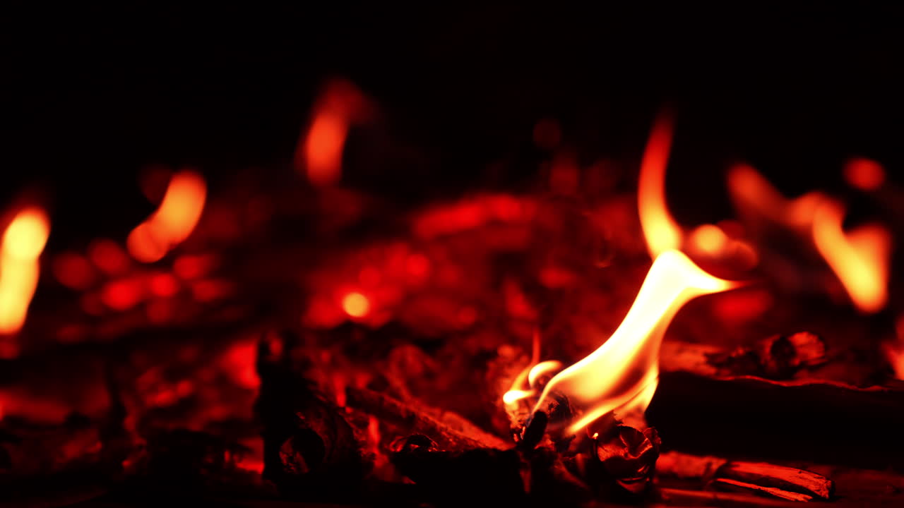 Remnants of wood burning out in the campfire. Red hot embers at backdrop in blur. Close up.