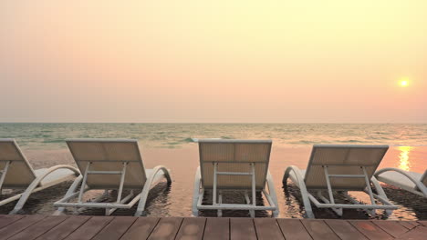 empty sun loungers positioned in the shallow incoming tide water facing a colorful sunset