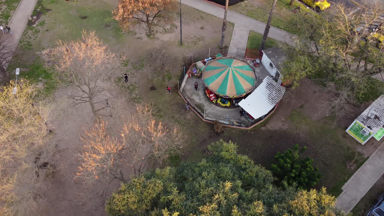 vista aérea del carrusel giratorio en el parque con niños felices jugando fútbol en la naturaleza