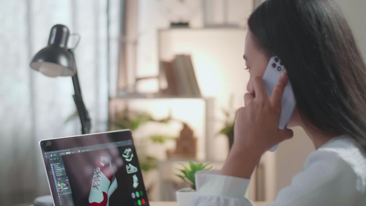mujer diseñando zapatos en una computadora portátil mientras habla por teléfono
