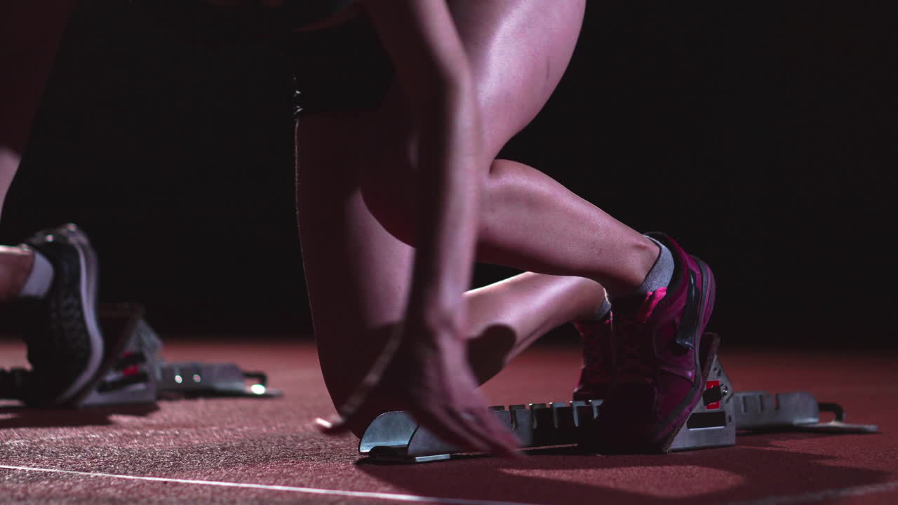 육상 트랙의 여자 달리기 선수들이 경주 전에 출발 블록에 앉아 있습니다. 슬로우 모션으로.