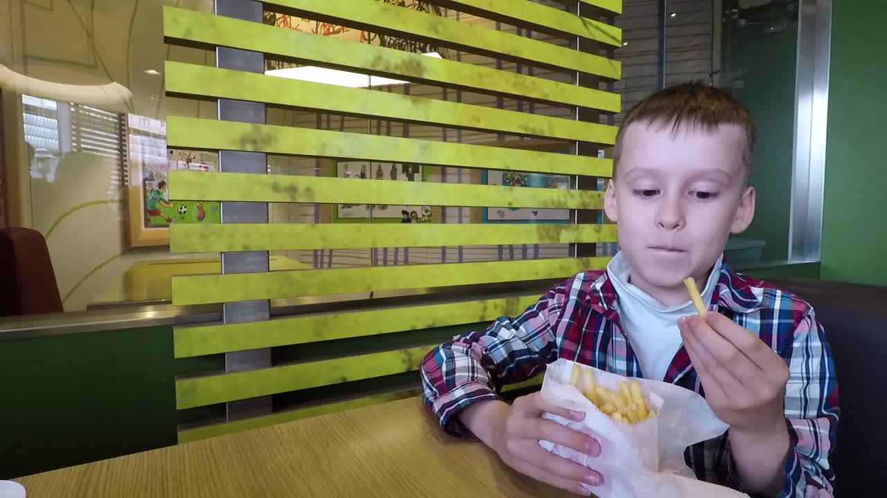 Ragazzo che mangia patatine fritte. Simpatico bambino che mangia fast food, patatine fritte al bar.