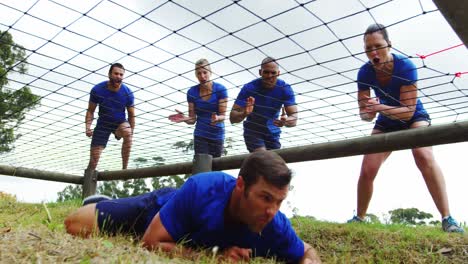 Fit-man-crawling-under-the-net-during-obstacle-course-while-fit-people-cheering-4k