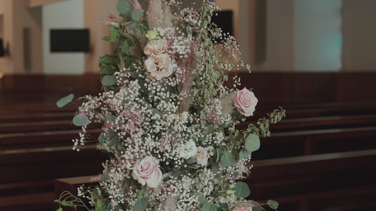 Close up of a delicate floral decoration with roses, eucalyptus, and baby's breath adorning a church interior