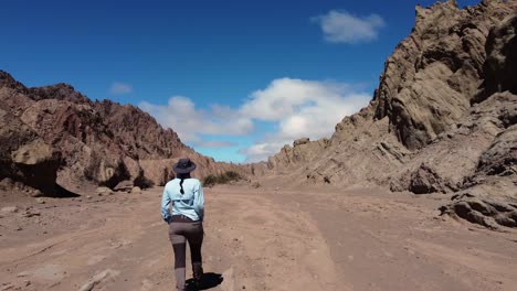 Latin-woman-with-braid-walks-up-Canon-del-Indio-sandstone-canyon,-ARG