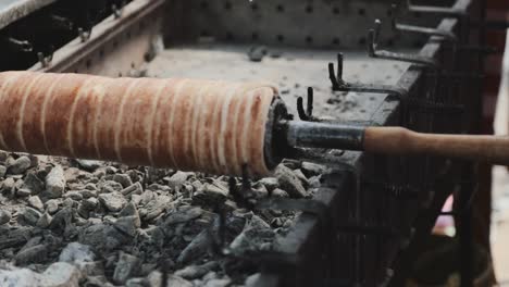 Making-a-hungarian-chimney-cake-above-the-glowing-ember-with-rotating-by-human-hands