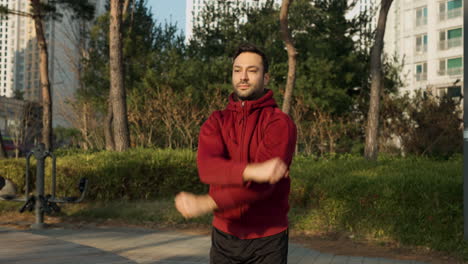 fit man in 30s warming up shoulder joints orbiting arms before exercises outdoors at apartment park sports ground