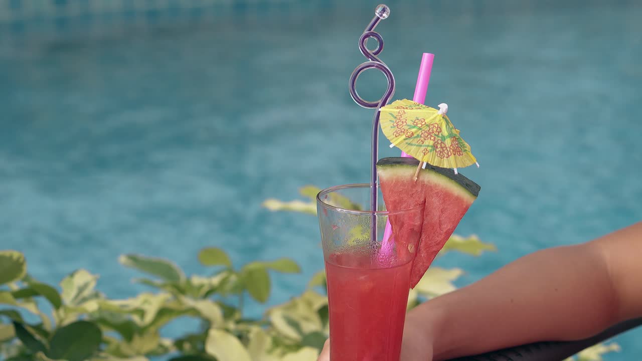 Cocktail med saftig vannmelon på kanten står mot basseng