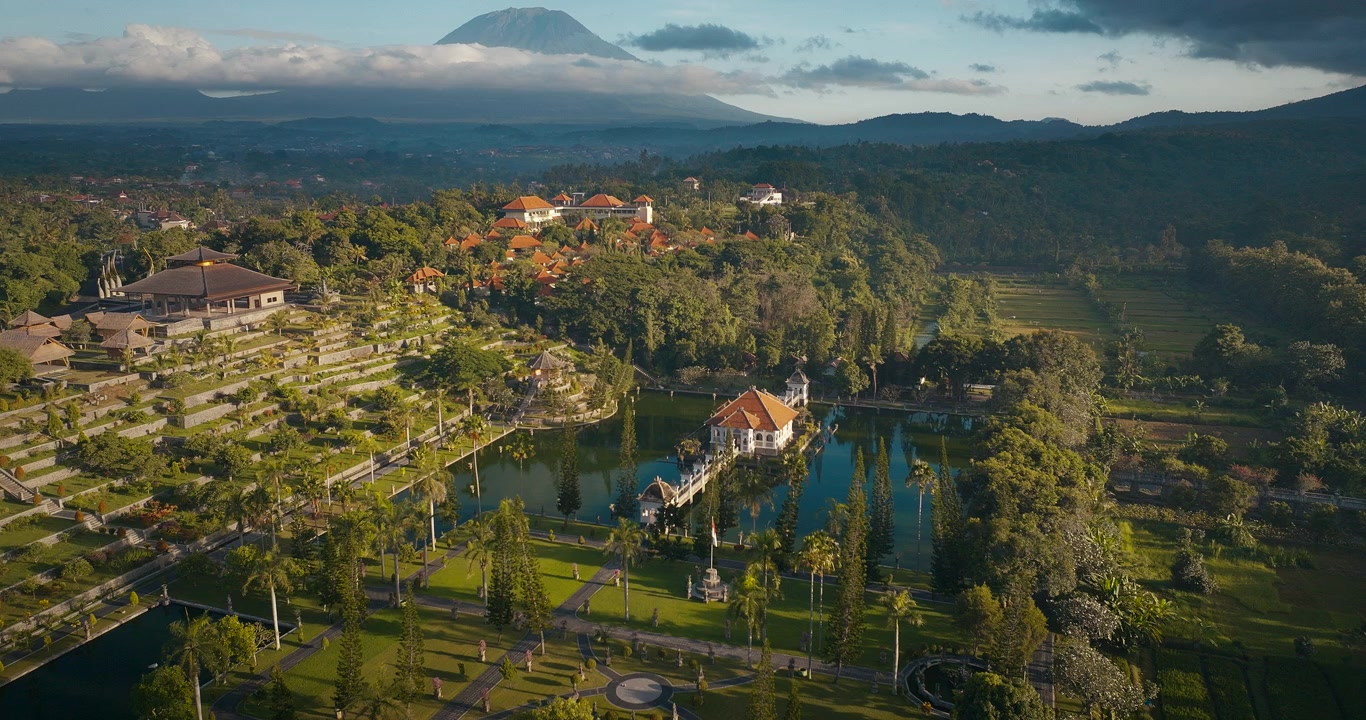 Istana dan taman kerajaan Taman Ujung di Bali timur dengan gunung berapi aktif Gunung Agung di latar belakang saat matahari terbenam, Bali. Rekaman drone.