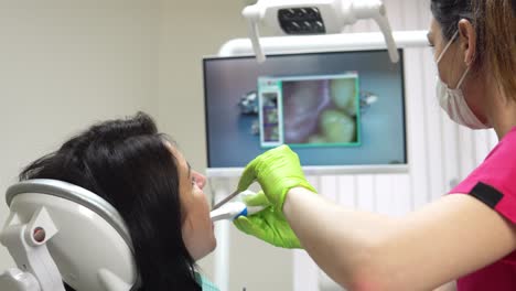 young female dentist examining the mouth of a patient with an intraoral camera and showing image on the screen. shot in 4k