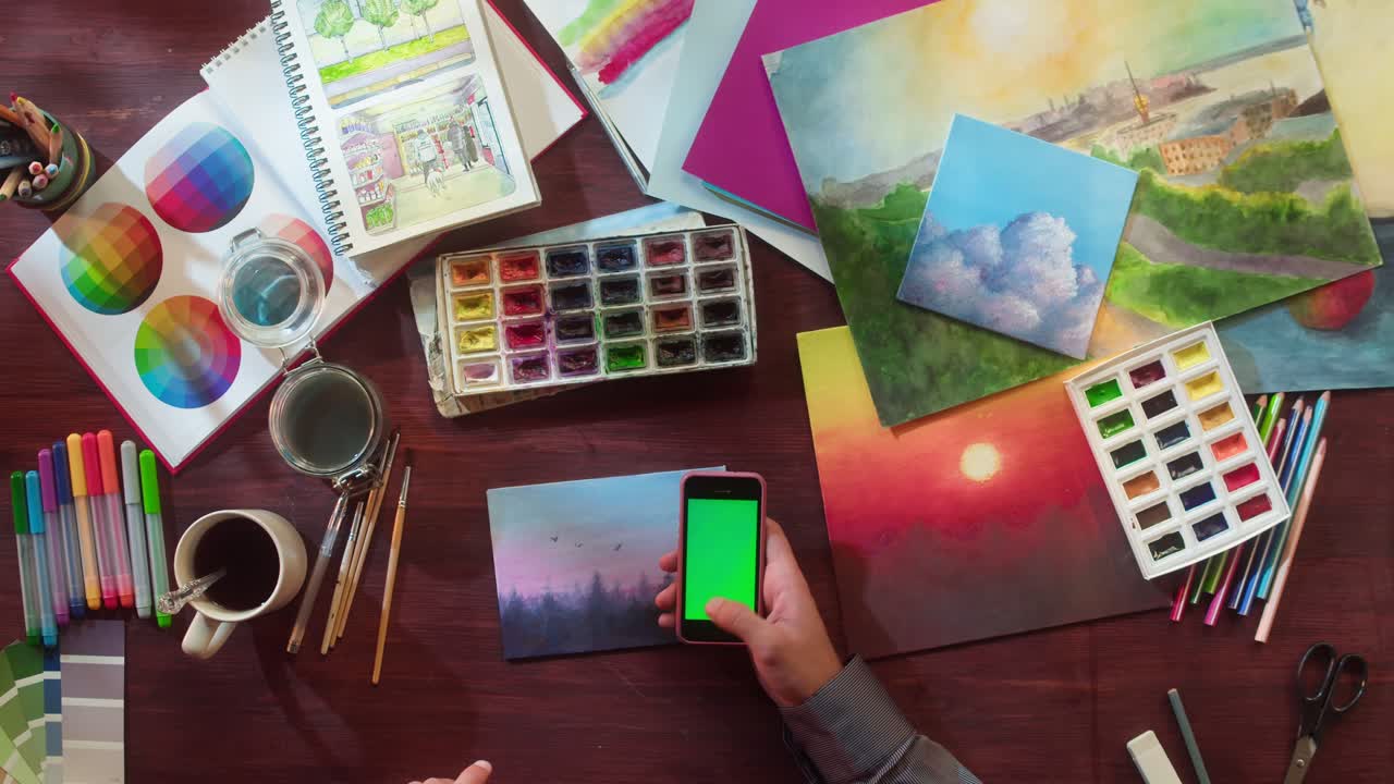 Artista pintando con acuarelas en un escritorio creativo con smartphone