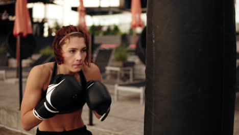 Junge-Athletische-Boxerin-In-Handschuhen,-Die-Mit-Händen-Und-Ellbogen-Gegen-Einen-Boxsack-Tritt.-Training-Draußen.-Boxerin-Trainiert-In-Boxhandschuhen.-In-4k-Gedreht