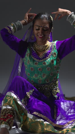 vertical video shot of female kathak dancer performing dance wearing traditional indian dress seated on floor in spotlight 2