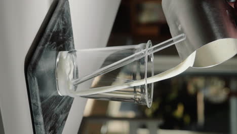 Vertical-Video-pouring-vegan-milk-into-glass-cup-with-glass-straw-in-slow-motion-close-up