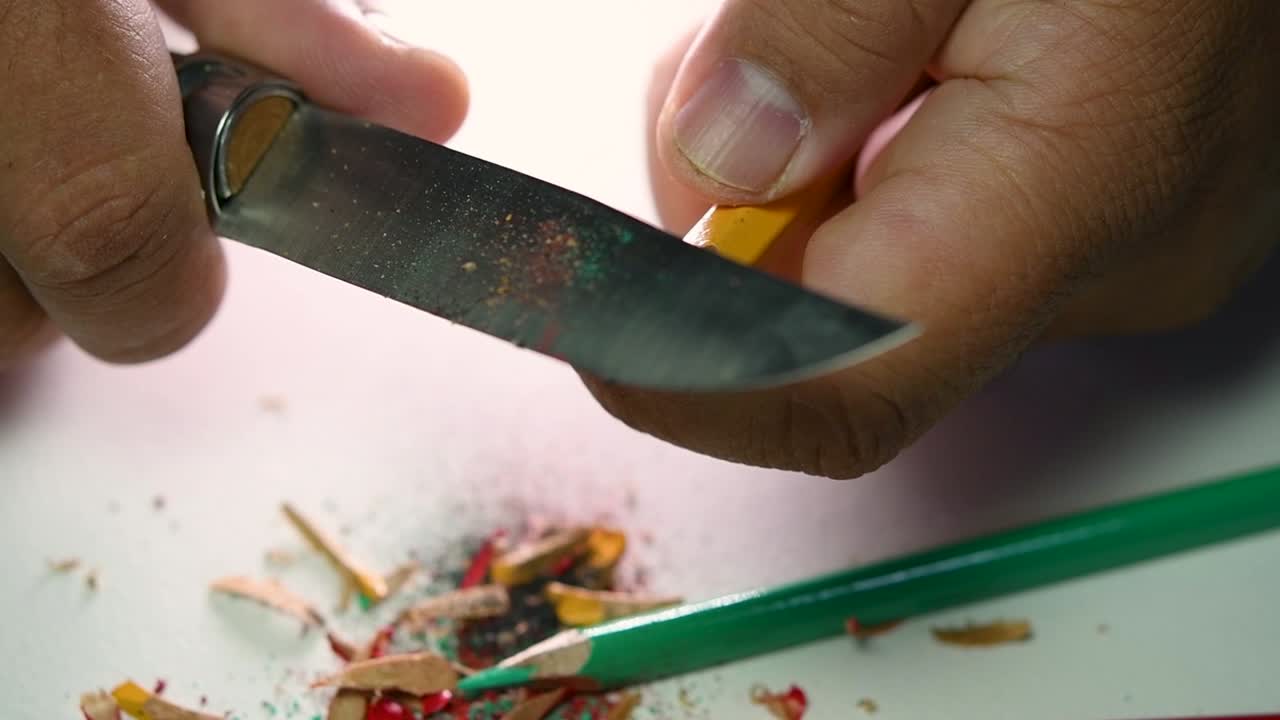 Opptak av hender som sakte spisser en blyant og noen fargeblyanter med en skarp kniv