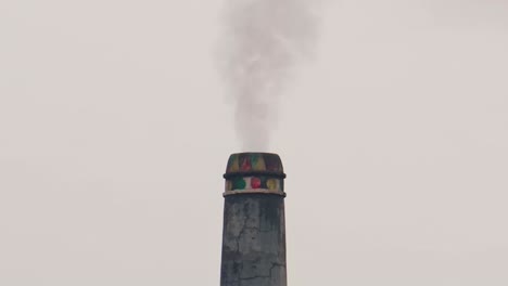 brick field chimney emits smoke against a grey sky