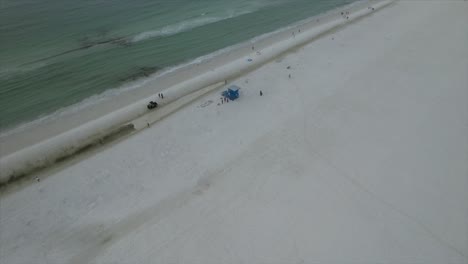 Drone-clip-panning-up-from-sandy-beach-to-the-ocean-shoreline-then-moving-towards-blue-beach-hut-on-the-shoreline