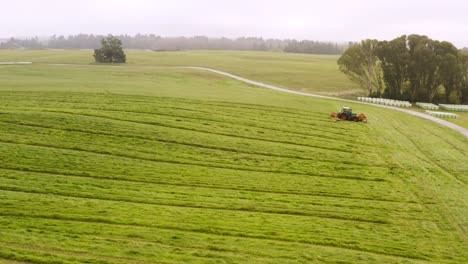 Tractor-mowing-lush-green-farm-field-creating-hay-for-cattle-food,-aerial