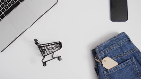 Video-of-smartphone-with-blank-screen,-laptop,-shopping-trolley-and-denim-trousers