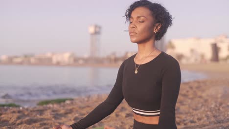 femme afro-américaine noire pratiquant la méditation du bouddhisme vipassana en position jambes croisées répandant l'amour et des ondes positives sur la plage de sable de barcelone espagne au lever du soleil