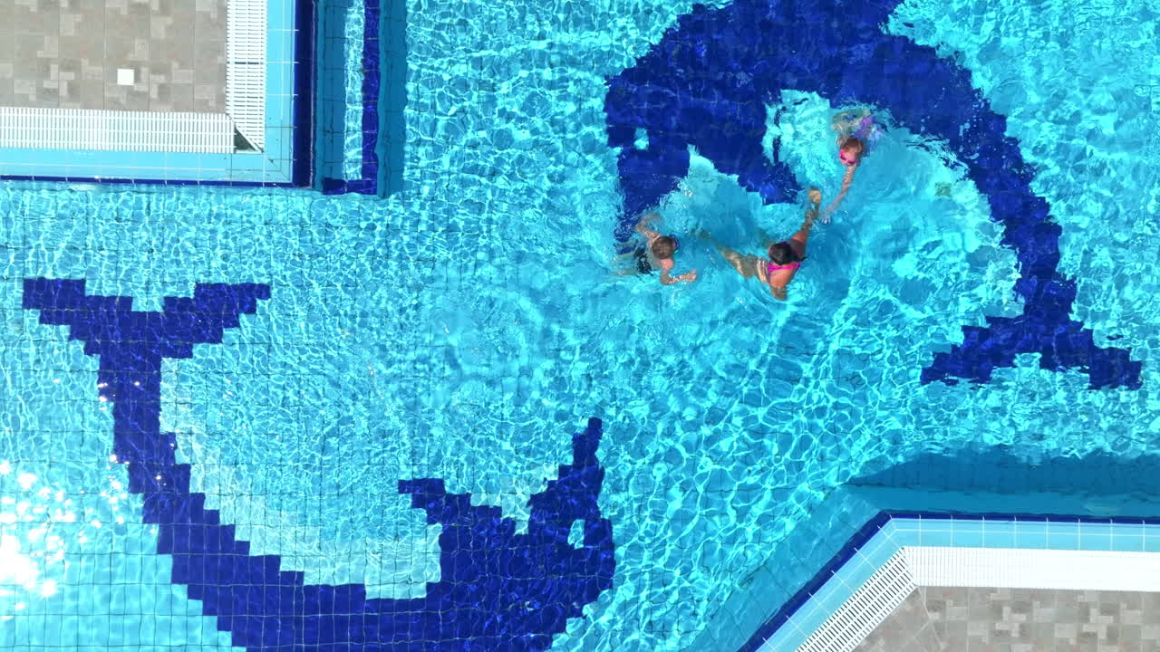 Droneoptagelse ovenfra af en mor og børn, der svømmer i en pool i solrige Grækenland.