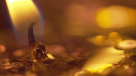 macro look at the golden flame from a candle and wick with sparkle and bokeh from the candles in the background - static