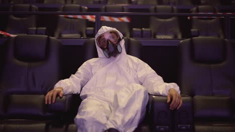 a man in white protection costume and respirator sitting alone at the cinema