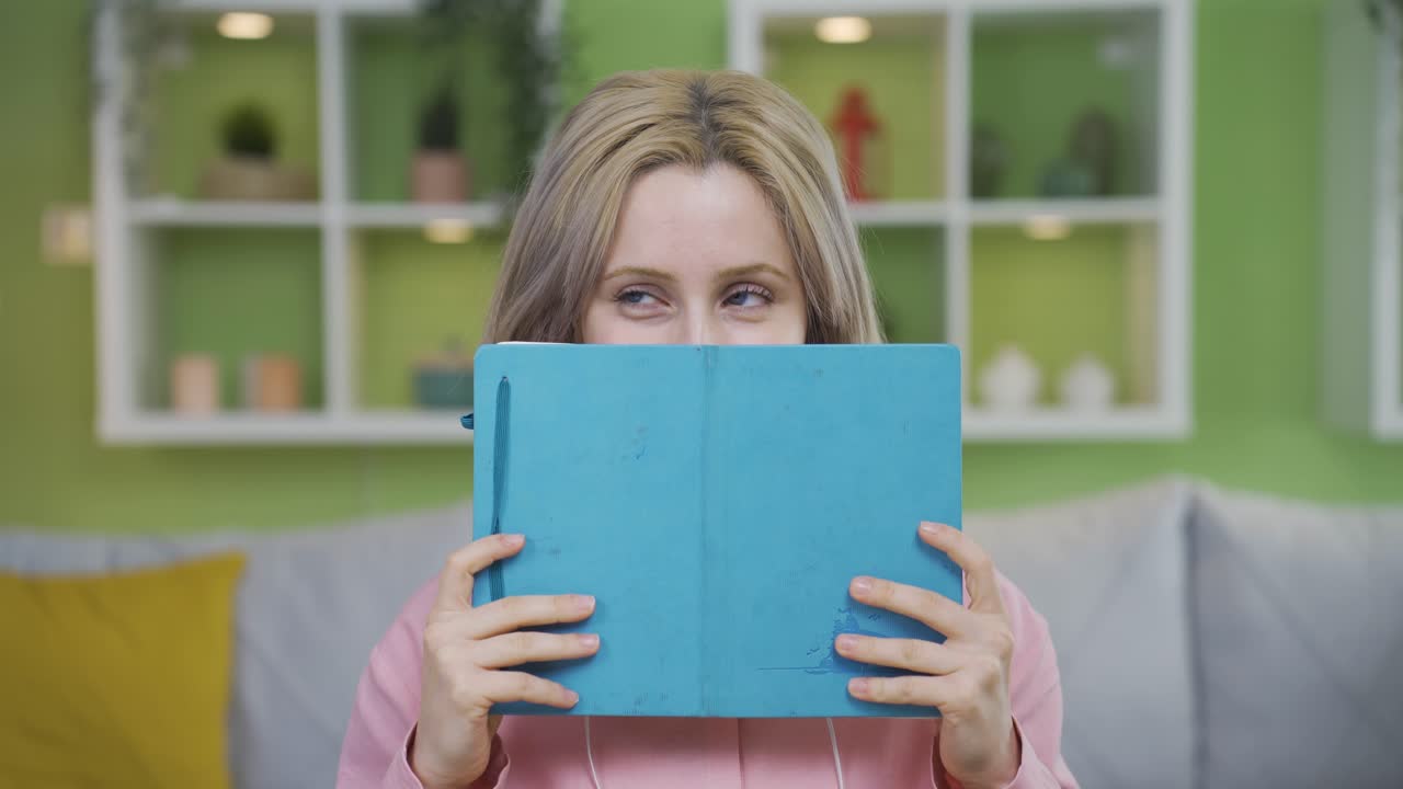 la chica divertida mirando desde la parte de atrás del libro sonríe a la cámara.