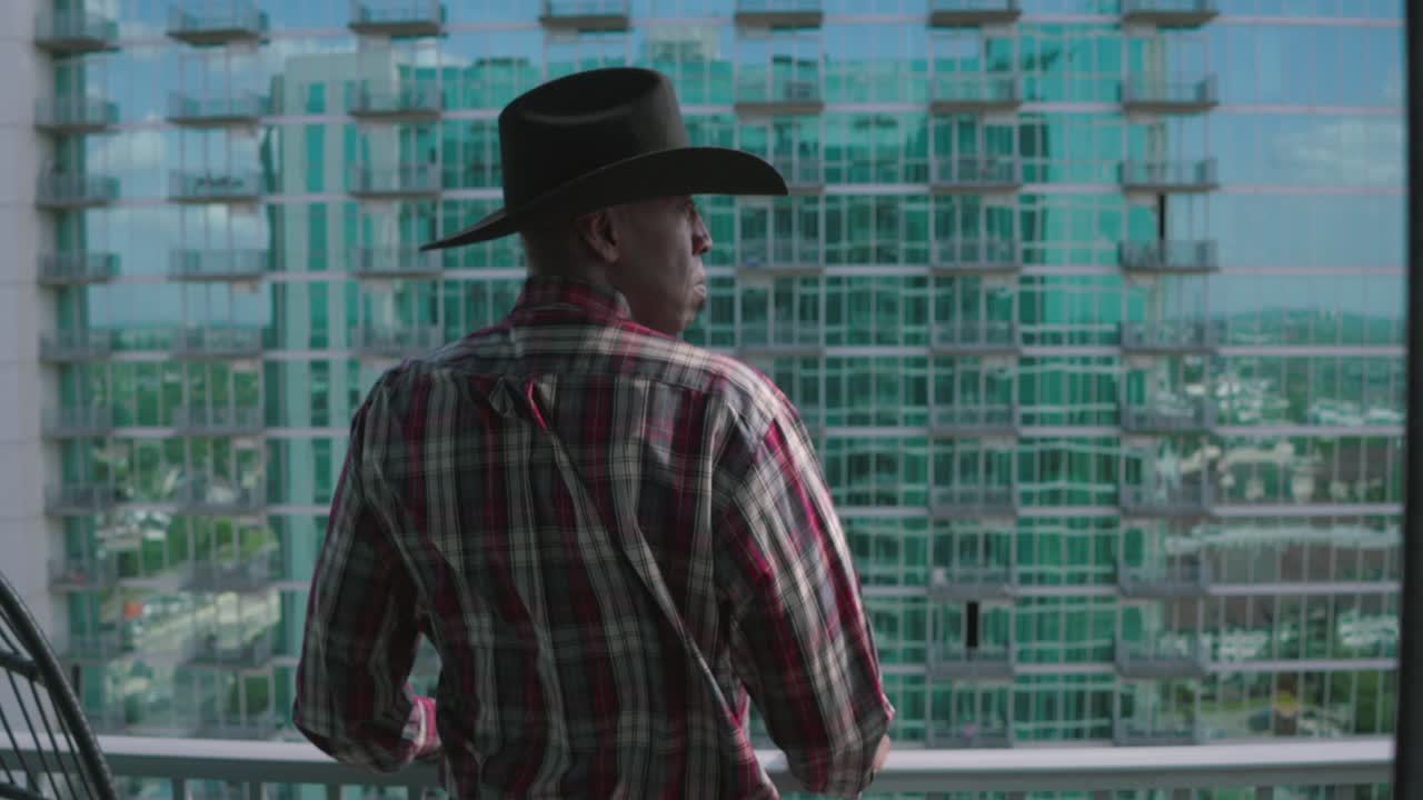 hombre negro con sombrero de vaquero negro mirando desde el balcón