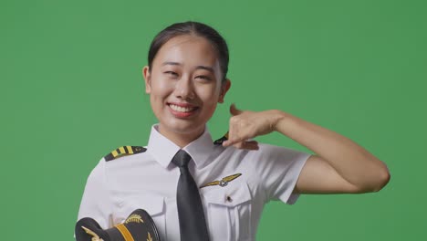 close up of asian woman pilot smiling and making call me gesture to camera while standing in the green screen background studio