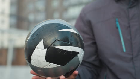 man skillfully rotates soccer ball in palm, showcasing precise control and focus, with urban high-rise buildings and mesh fence in background