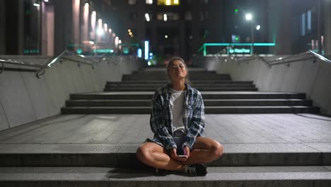 joven usando un teléfono inteligente por la noche en las escaleras de la ciudad