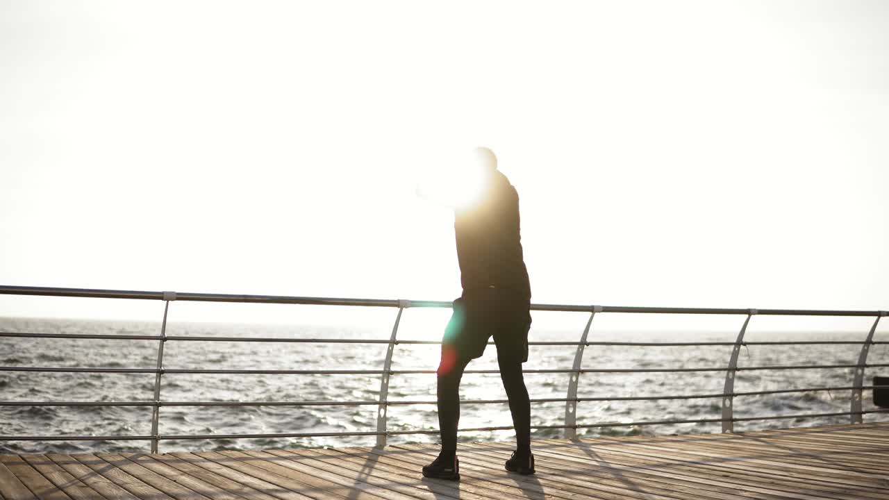 Male silhouette stretching out on the dock near the seaside. Beautiful sunrise in the morning.