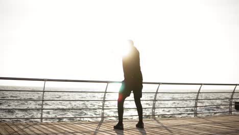 Male-silhouette-stretching-out-on-the-dock-near-the-seaside.-Beautiful-sunrise-in-the-morning.