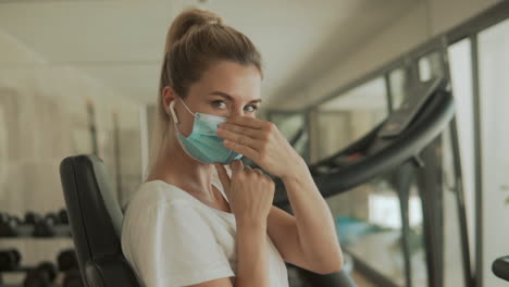 Young-athlete-female-with-face-mask-and-looks-to-camera-in-the-gym.-Close-up.