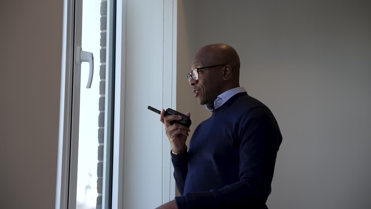 Bald Black businessman communicating through a walkie talkie in a modern office setting