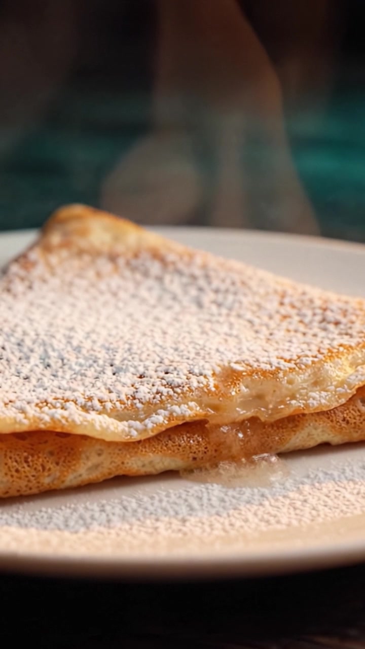 Deliciously Whipped Crepe with Dusting of Powdered Sugar, Plated Elegantly and Steaming, Perfect for Any Dessert Lover or Culinary Enthusiast to Savor.