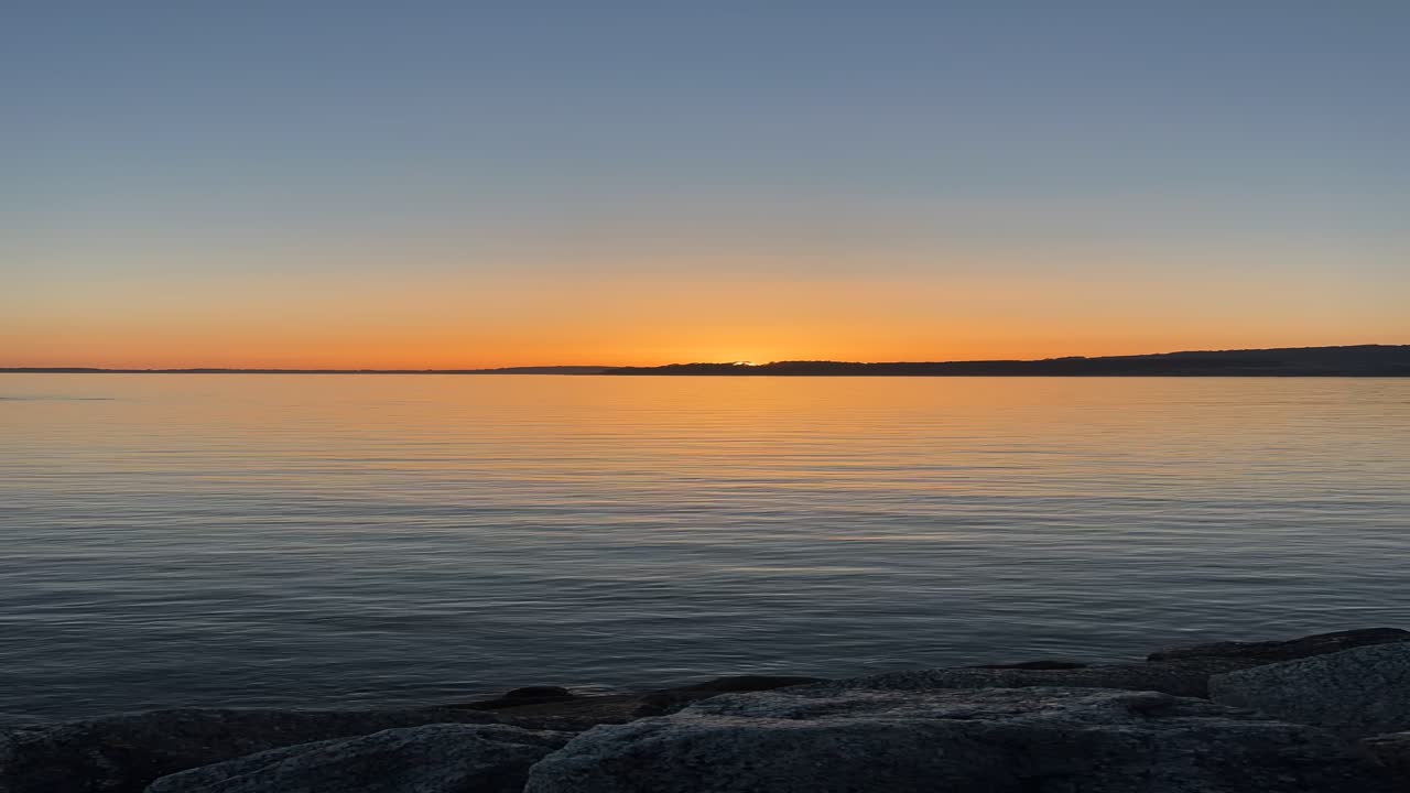 Time lapse shot of orange sunset taken from coastline during evening.