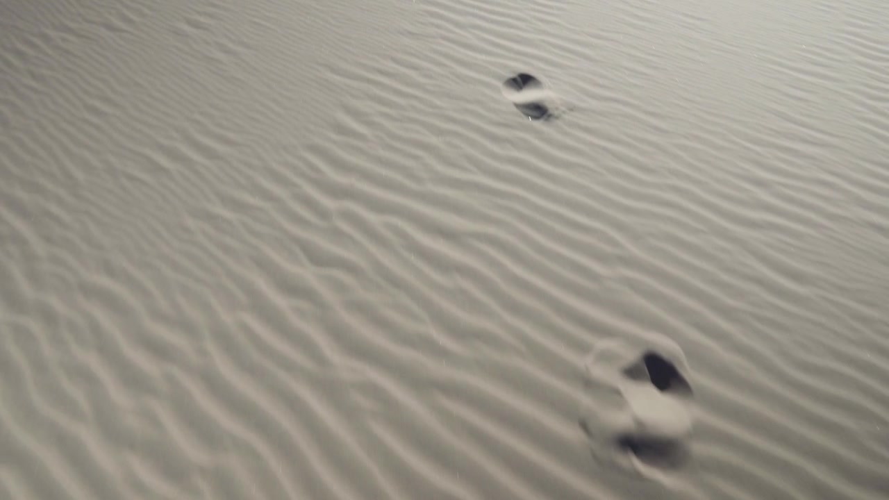 4k stabilised dolly shot following footsteps in sand dunes with wind