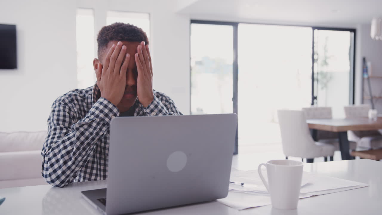 adolescente negro deprimido con la cabeza en las manos usando una computadora portátil en casa, de cerca