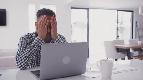 depressed black teenage boy with head in hands using a laptop computer at home, close up