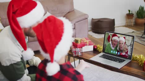 Hombre-Caucásico-Con-Hijo-Usando-Gorros-De-Papá-Noel-En-Video-Chat-Portátil-Durante-La-Navidad-En-Casa