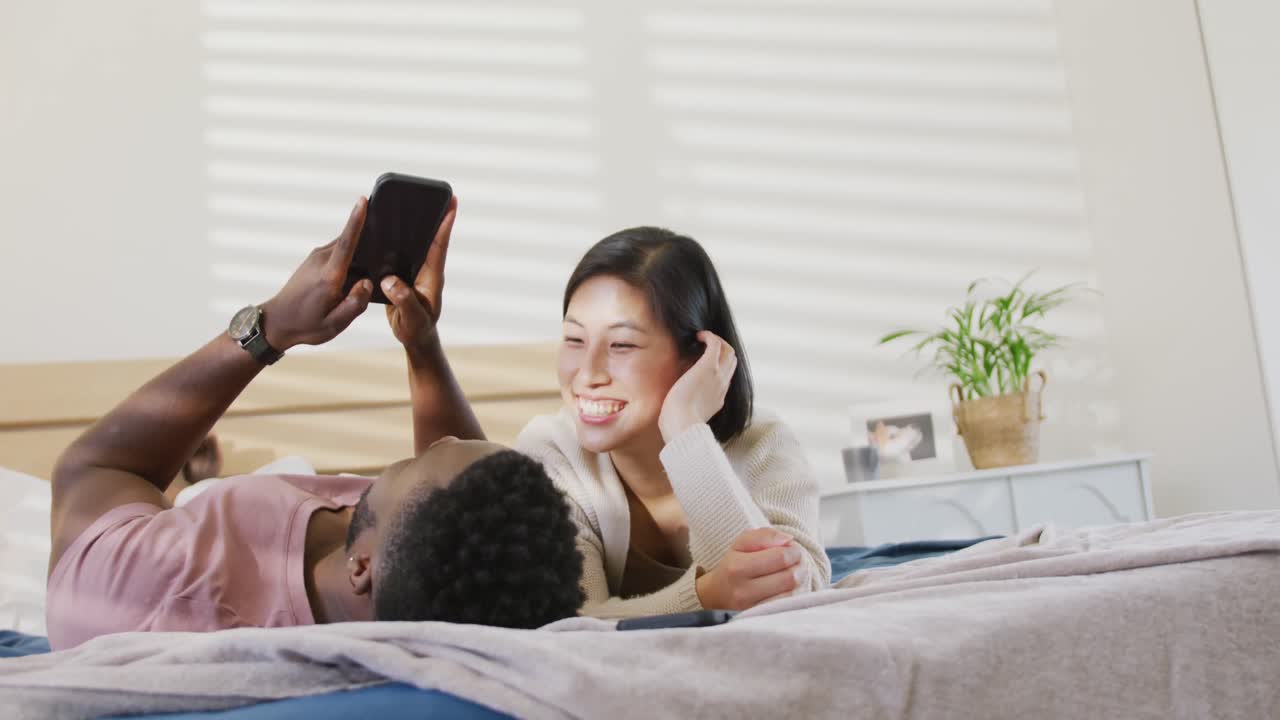 스마트 폰을 사용하고 침실에 누워있는 다양한 행복한 커플