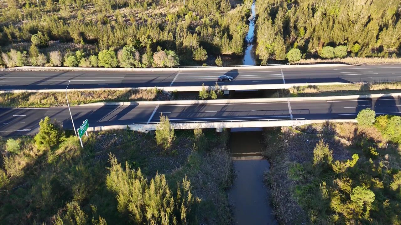 High angle drone shot of vehicles crossing a modern bridge over a creek in Gulmarrad.