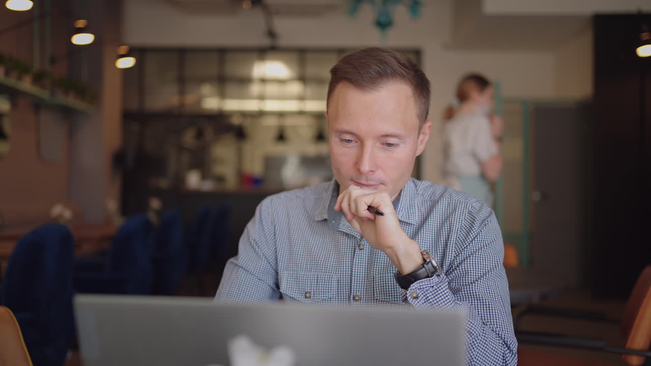 Close-up portrait of ponder young man in office. Designer plans his work and holding a pencil in his hand. Shooting is slow motion from below. Thoughtful serious man sit with laptop thinking solution