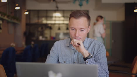 close-up portrait of ponder young man in office. designer plans his work and holding a pencil in his hand. shooting is slow motion from below. thoughtful serious man sit with laptop thinking solution