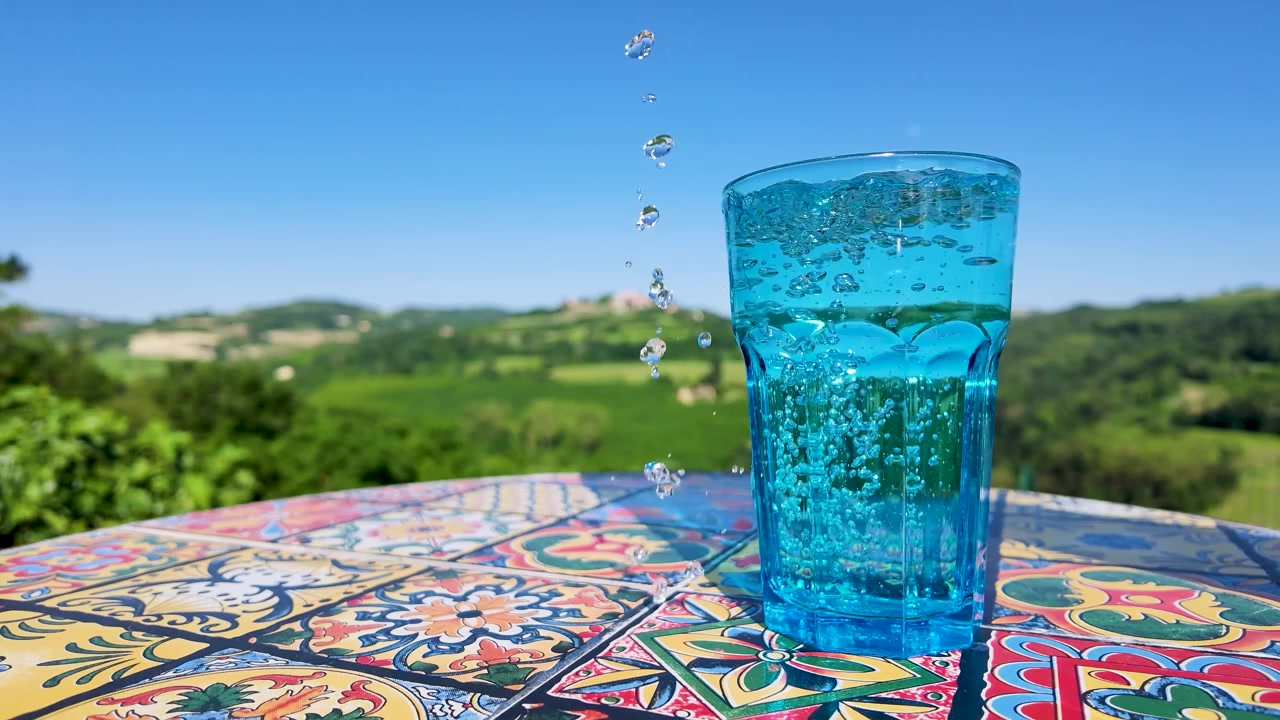 Water Being Poured into a Blue Glass on a Colorful Table with a Scenic View