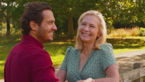 Mature-Mother-With-Mixed-Race-Adult-Son-Leaning-On-Fence-Walking-In-Summer-Countryside